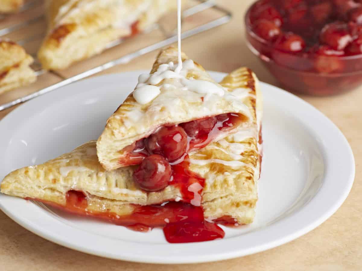 Glaçage arrosé sur deux chaussons aux cerises sur une assiette.