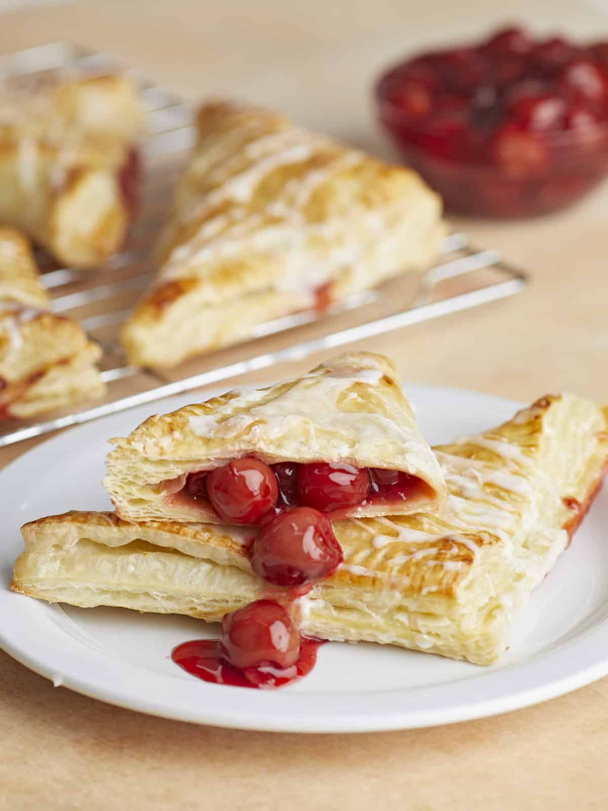 Deux chaussons aux cerises sur une assiette, un coupé en deux avec la garniture qui coule.