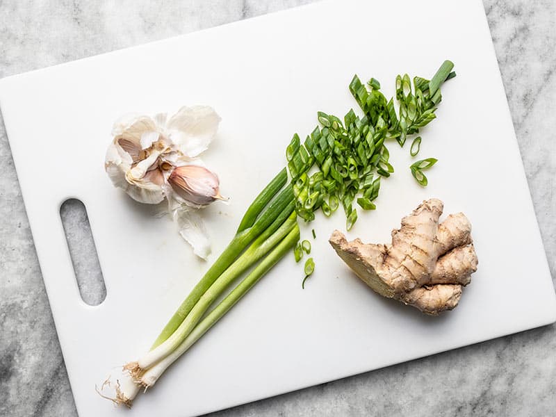 Ail, oignon vert tranché et gingembre sur une planche à découper.