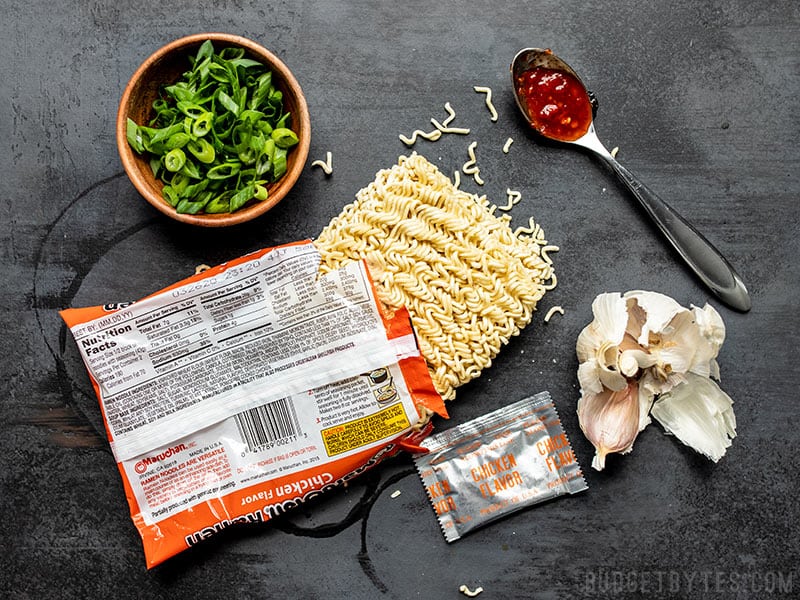 Un paquet ouvert de ramen instantané avec d'autres ingrédients autour, notamment des oignons verts, de la pâte de chili et de l'ail.