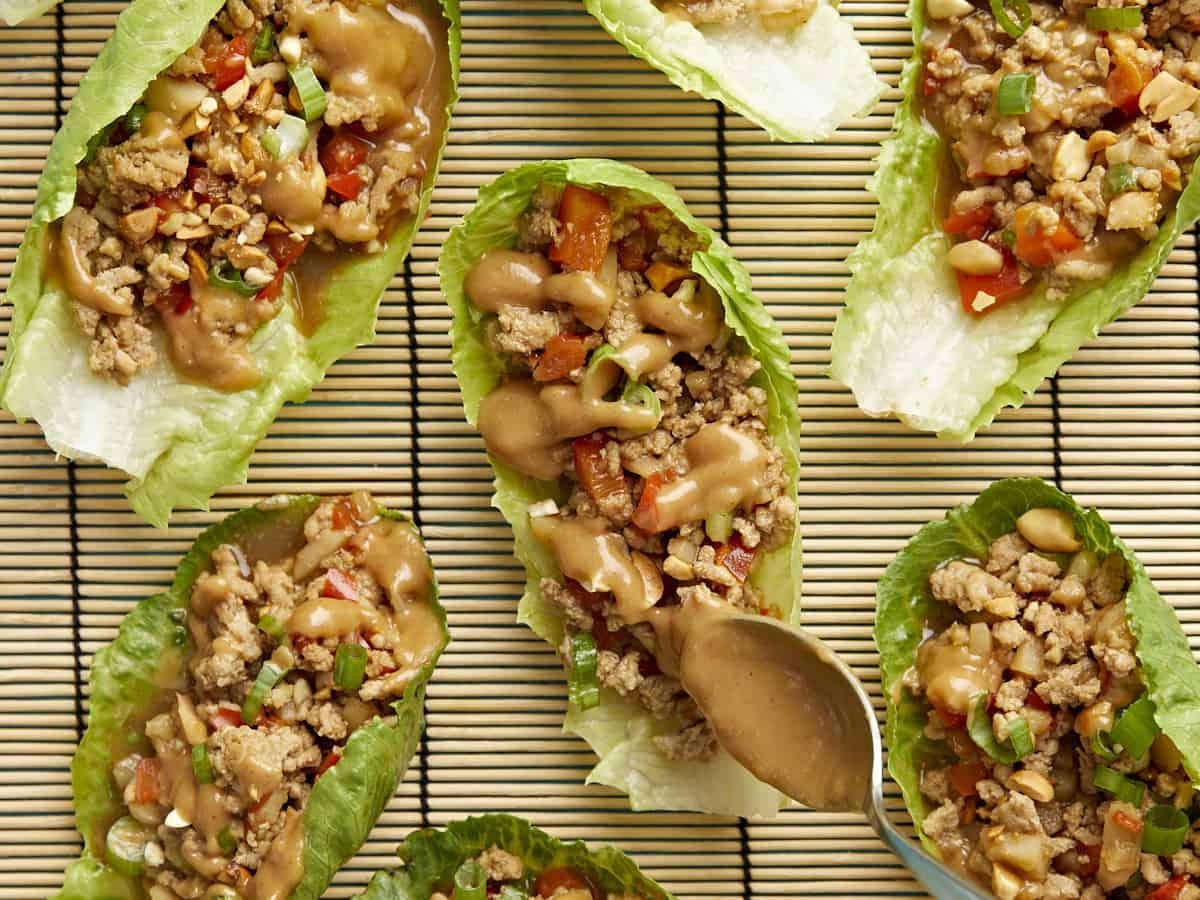 Très gros plan de roulés de laitue au poulet arrosés de vinaigrette aux arachides et au citron vert.