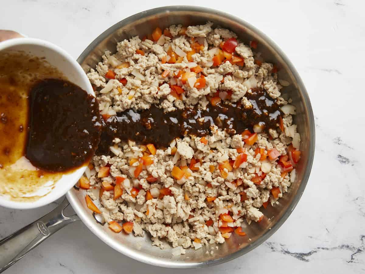 Mélange de sauce asiatique versé sur du poulet et des légumes cuits.