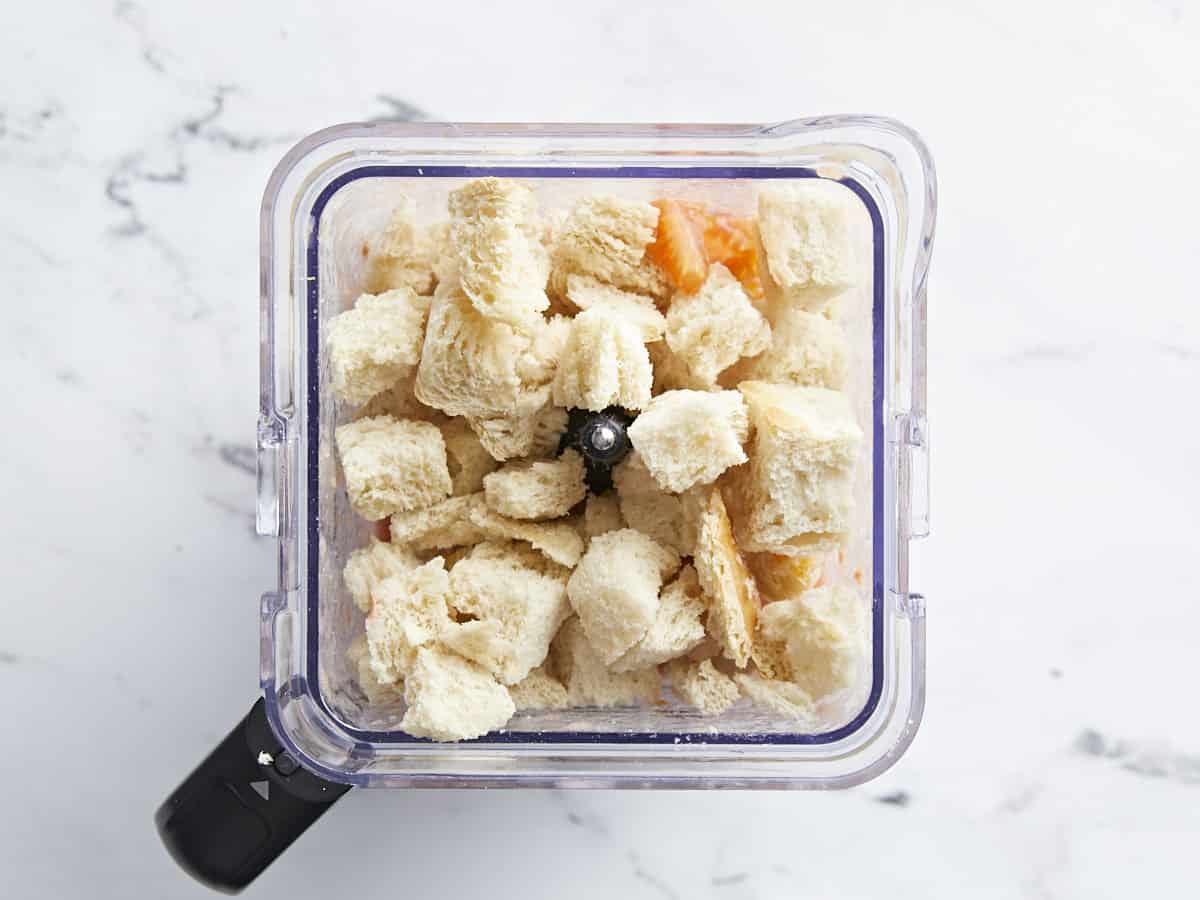 Plan aérien d'ingrédients Salmorejo garnis de pain en cubes dans un bol mixeur.