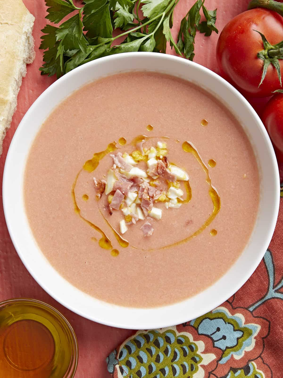 Plan aérien d'un bol blanc de Salmorejo garni d'un filet d'huile d'olive, d'œufs durs hachés et de jambon croustillant émietté.