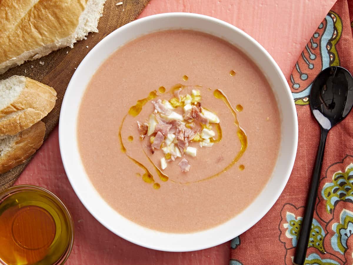 Plan aérien d'un bol blanc de Salmorejo garni d'un filet d'huile d'olive, d'œufs durs hachés et de jambon croustillant émietté.