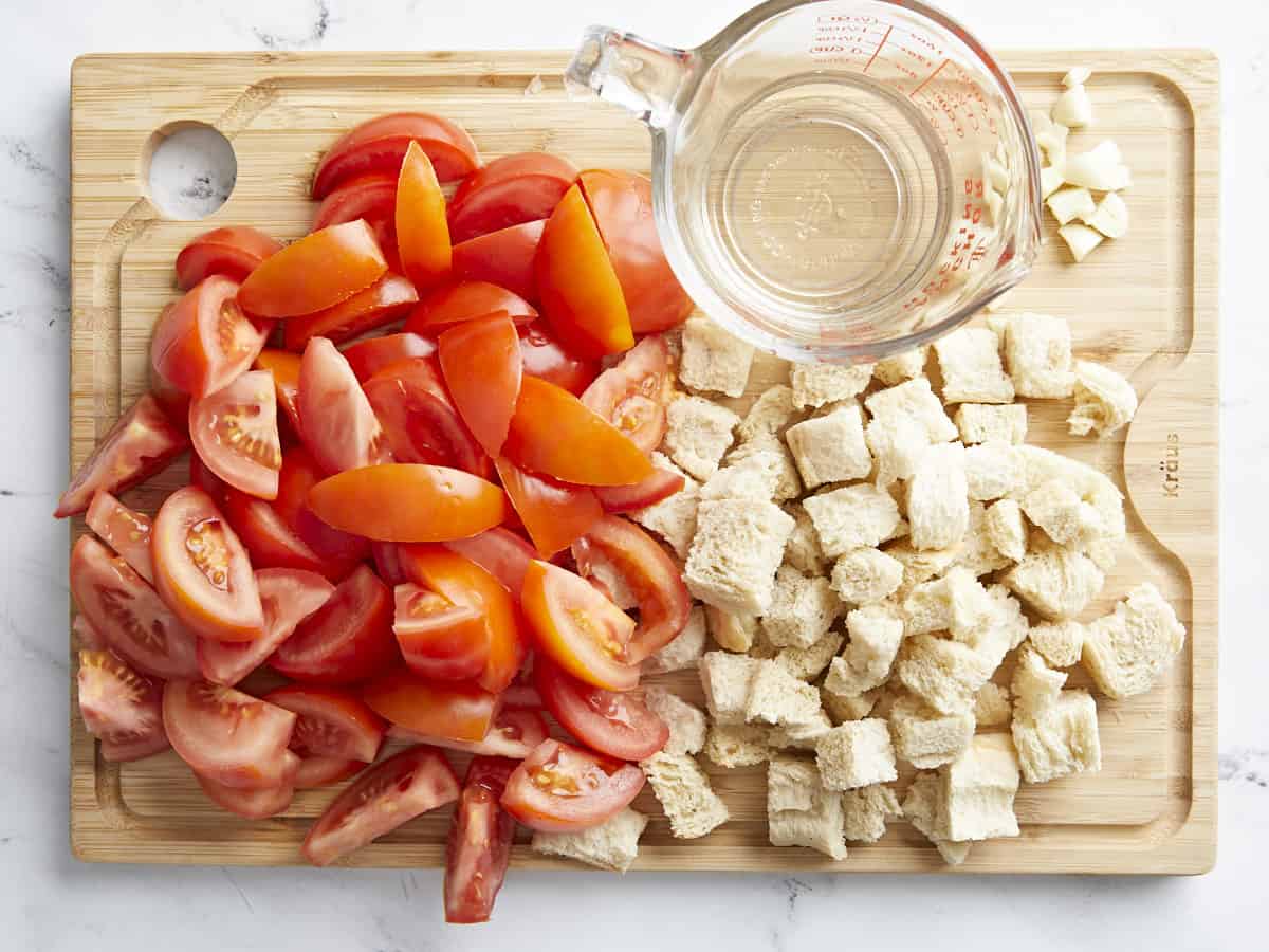 Photo aérienne des principaux ingrédients de Salmorejo : tomates fraîches hachées, pain d'un jour haché et eau, sur une planche à découper en bois.
