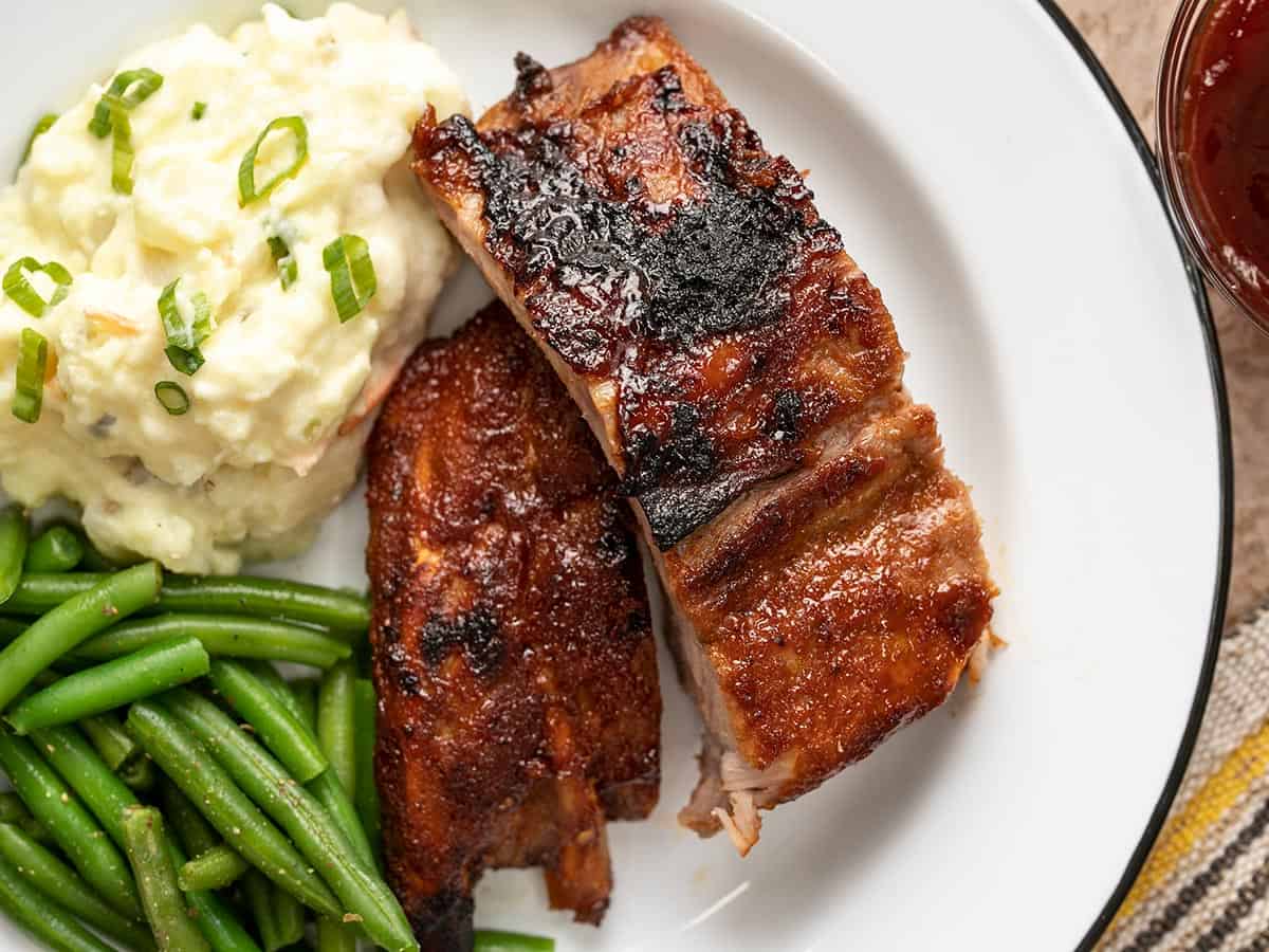 Couper les côtes levées sur une assiette blanche avec de la purée de pommes de terre et des haricots verts.