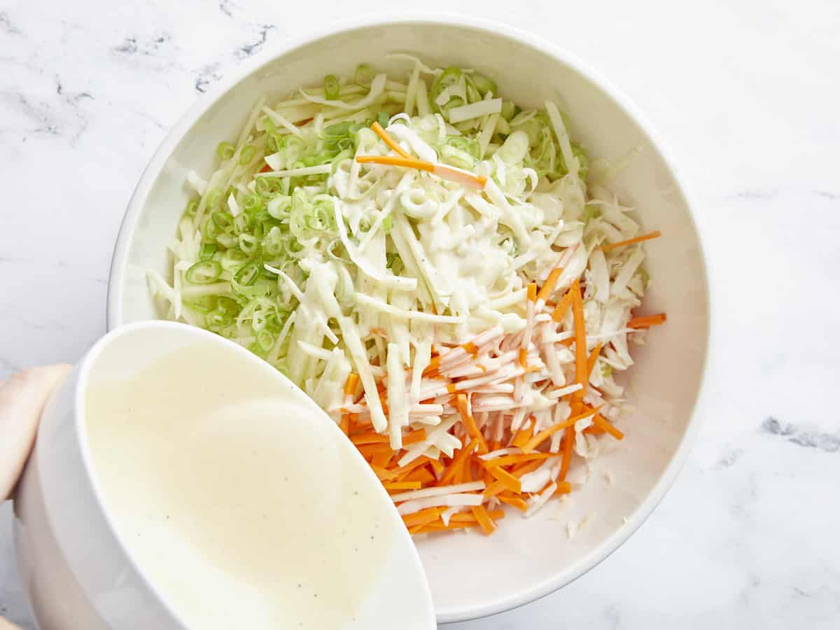 Vinaigrette versée sur le bol de légumes râpés.