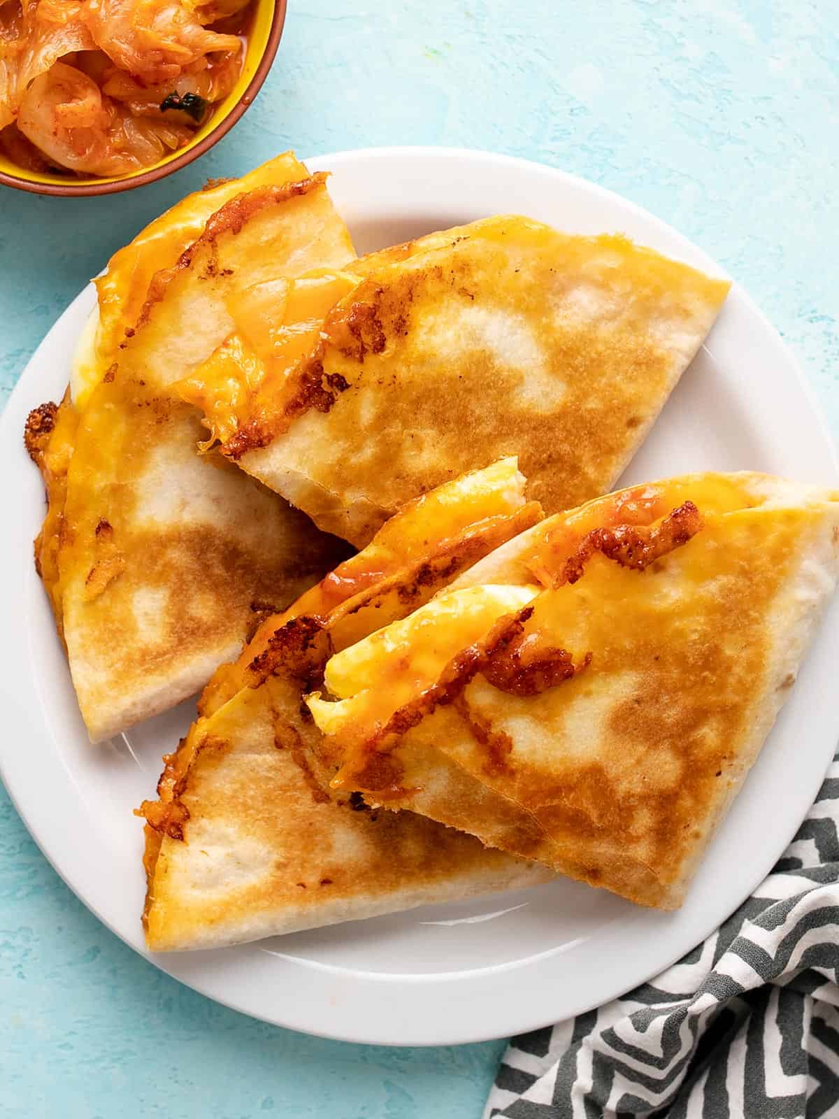 Quesadillas au fromage sur une assiette avec un bol de kimchi sur le côté.