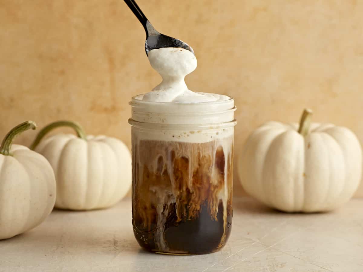 Une cuillère soulève un peu de mousse froide et de crème sucrée du dessus du verre de café glacé.