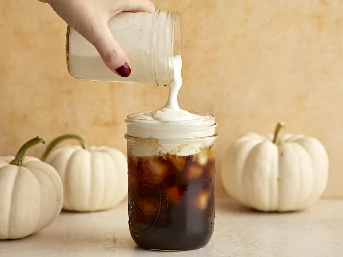 Mousse froide à la crème sucrée versée sur un pot rempli de café glacé.