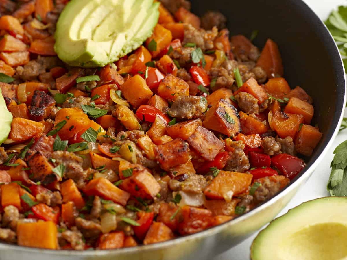Vue latérale du hachis de patate douce dans une poêle avec des tranches d'avocat sur le dessus.