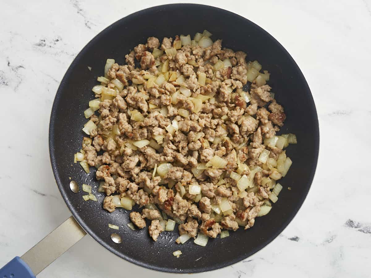 Saucisse dorée et oignon dans une poêle antiadhésive.