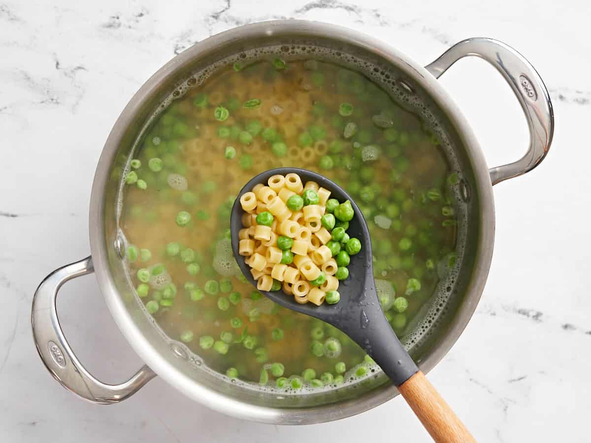 Pâtes cuites et petits pois dans une casserole avec une cuillère en soulevant un peu de l'eau.