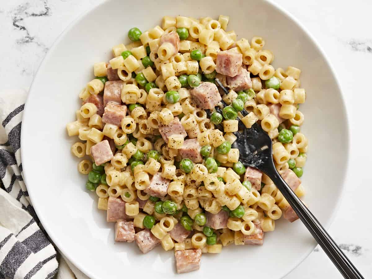 Vue aérienne d'un bol rempli de pâtes aux petits pois et au jambon et d'une fourchette.