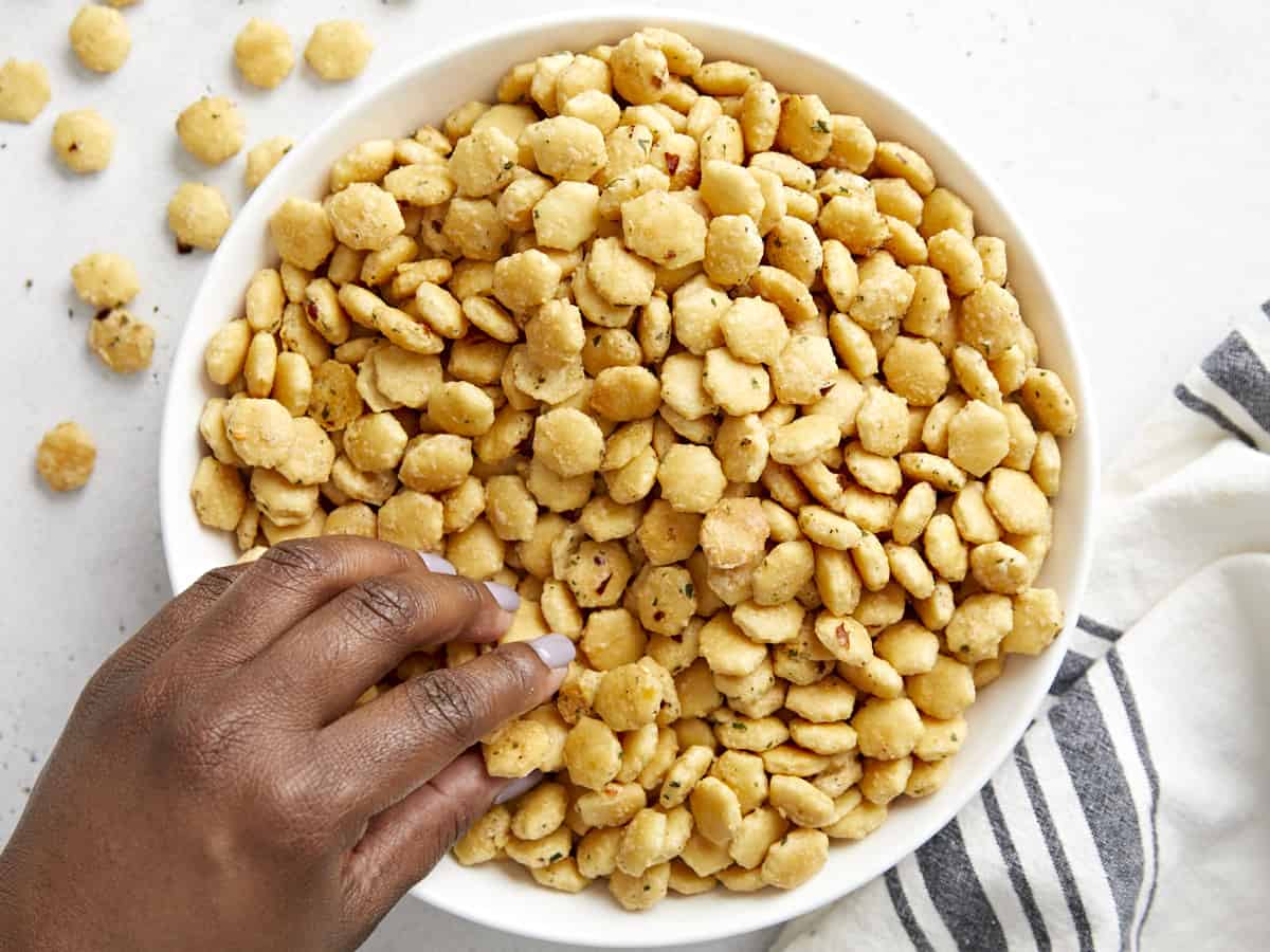 Craquelins aux huîtres ranch dans un bol de service blanc avec une main en saisissant quelques-uns.