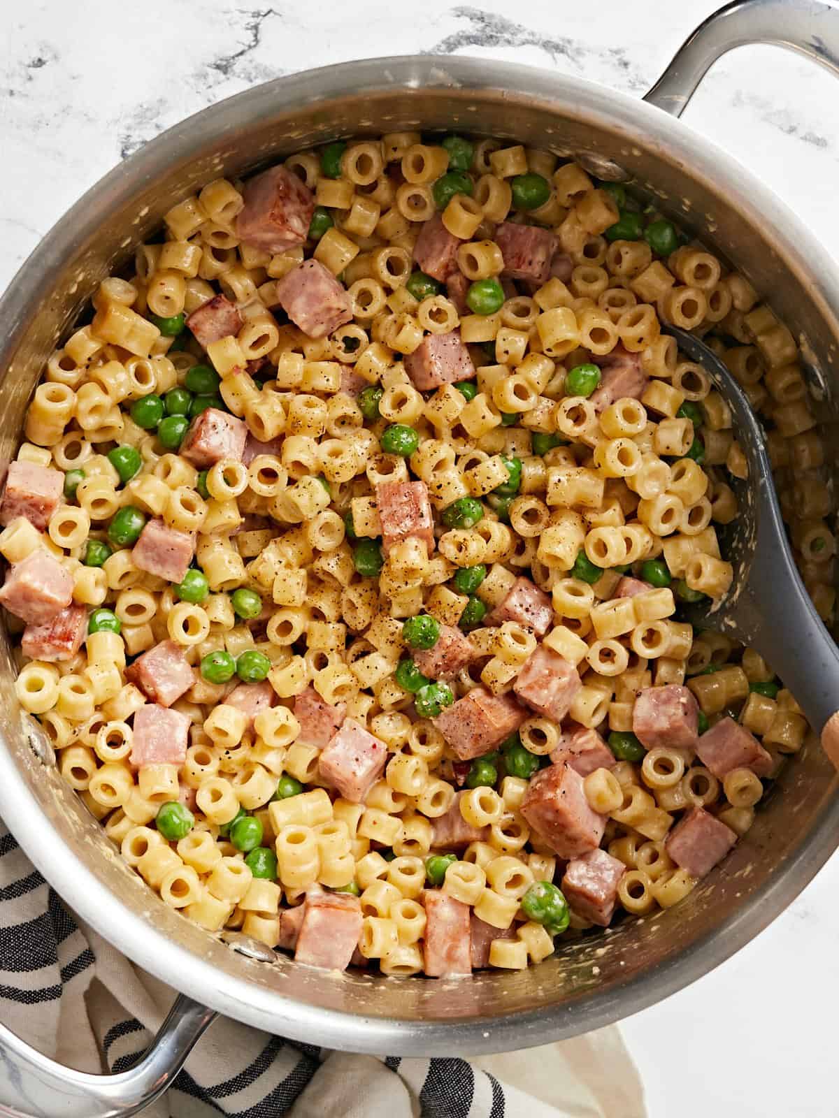 Vue aérienne d'une marmite pleine de pâtes aux petits pois et au jambon, une cuillère sur le côté.
