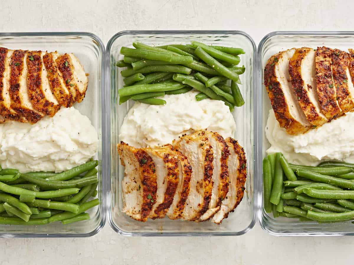 Poitrine de poulet Air Fryer tranchée dans des contenants de préparation de repas avec des haricots verts et de la purée de pommes de terre sur le côté.