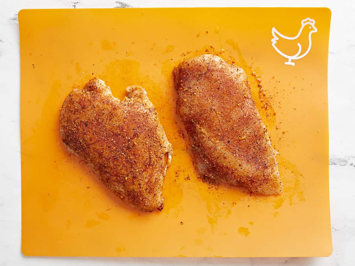 Poitrines de poulet assaisonnées sur une planche à découper.