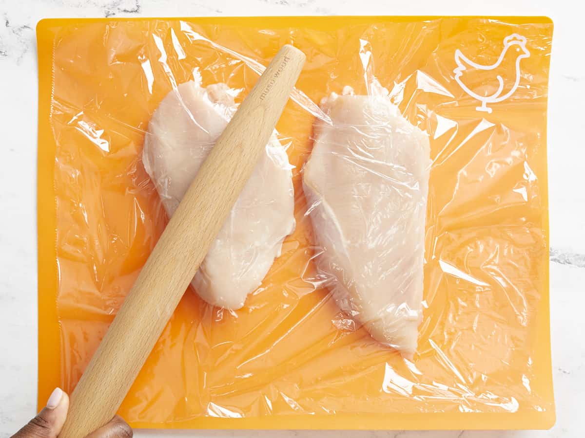 poitrines de poulet sur une planche à découper pilées avec un rouleau à pâtisserie.