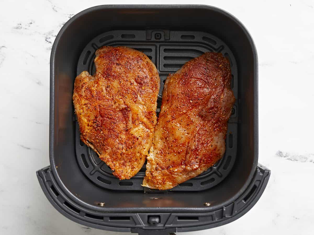 Poitrines de poulet non cuites ajoutées à un panier de friteuse à air.