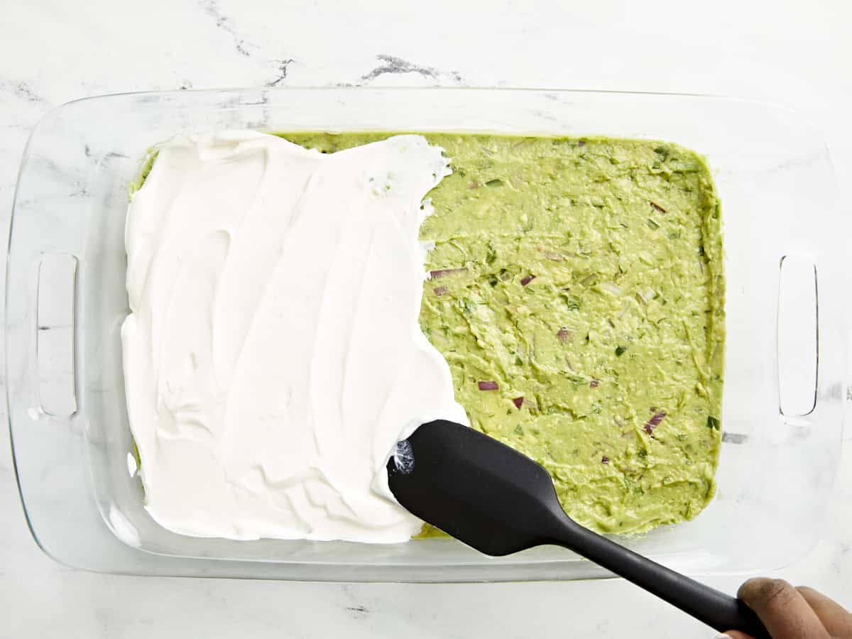 Crème sure étalée sur le guacamole avec une spatule noire.