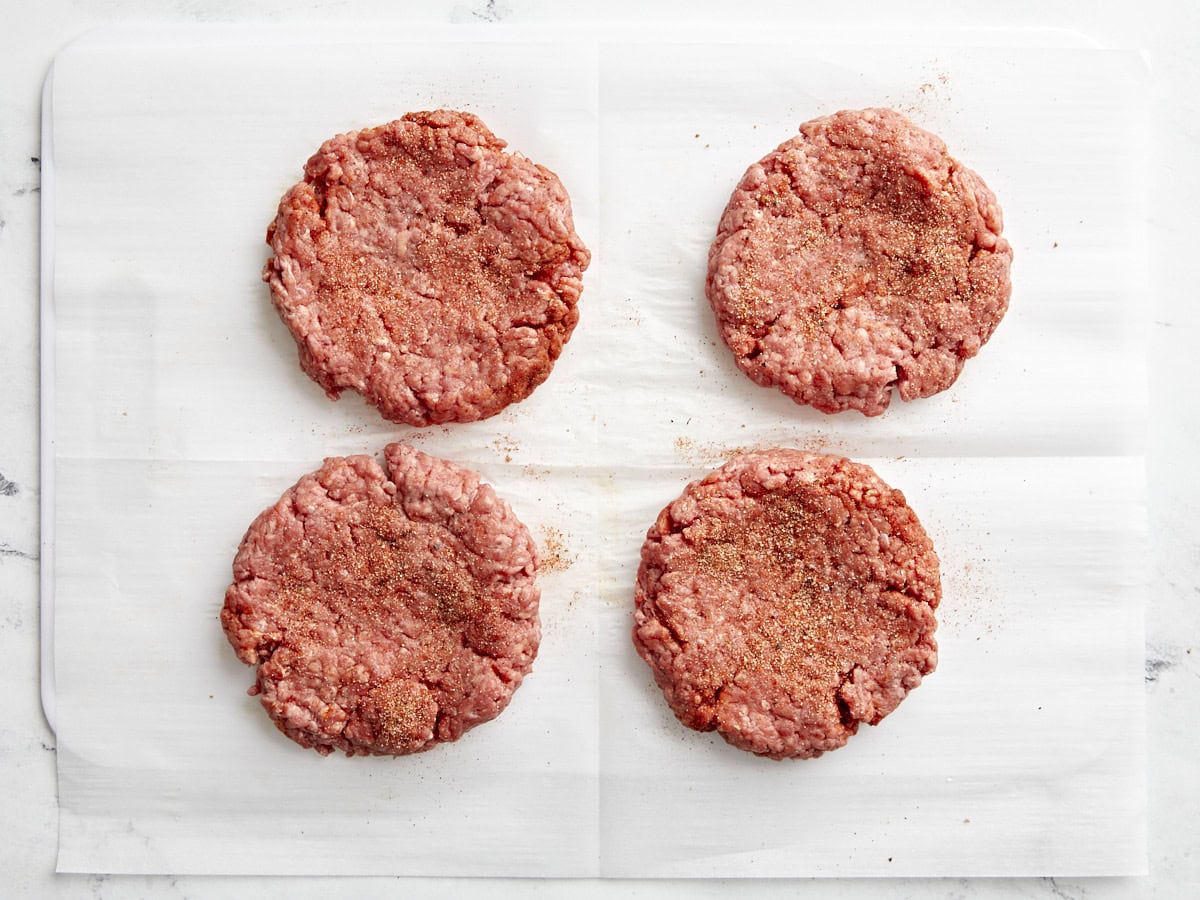Quatre galettes de hamburger au bœuf haché avec assaisonnement pour hamburger sur le dessus.