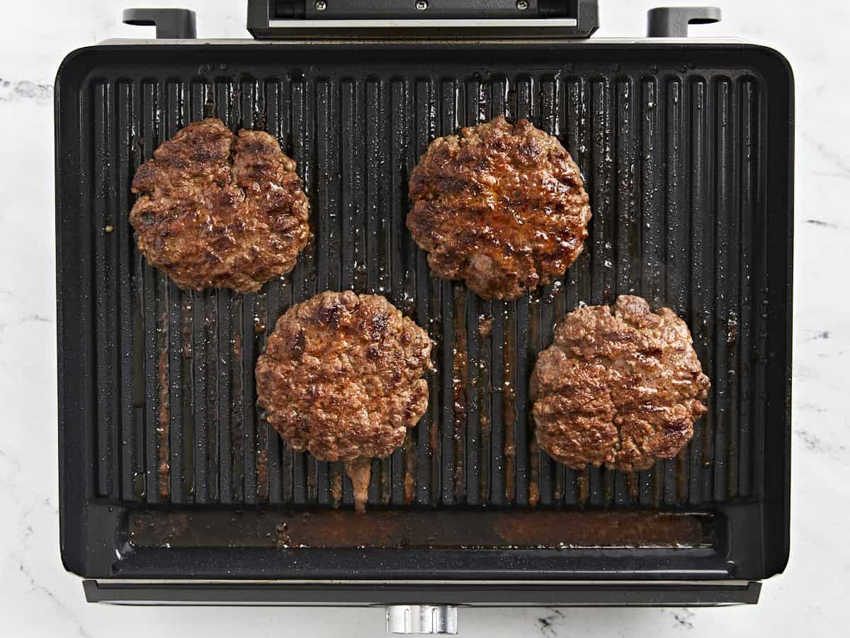 Des hamburgers retournés sur un grill.