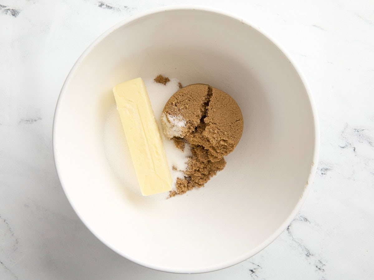 un bâton de beurre, de sucre blanc et de cassonade dans un bol blanc.