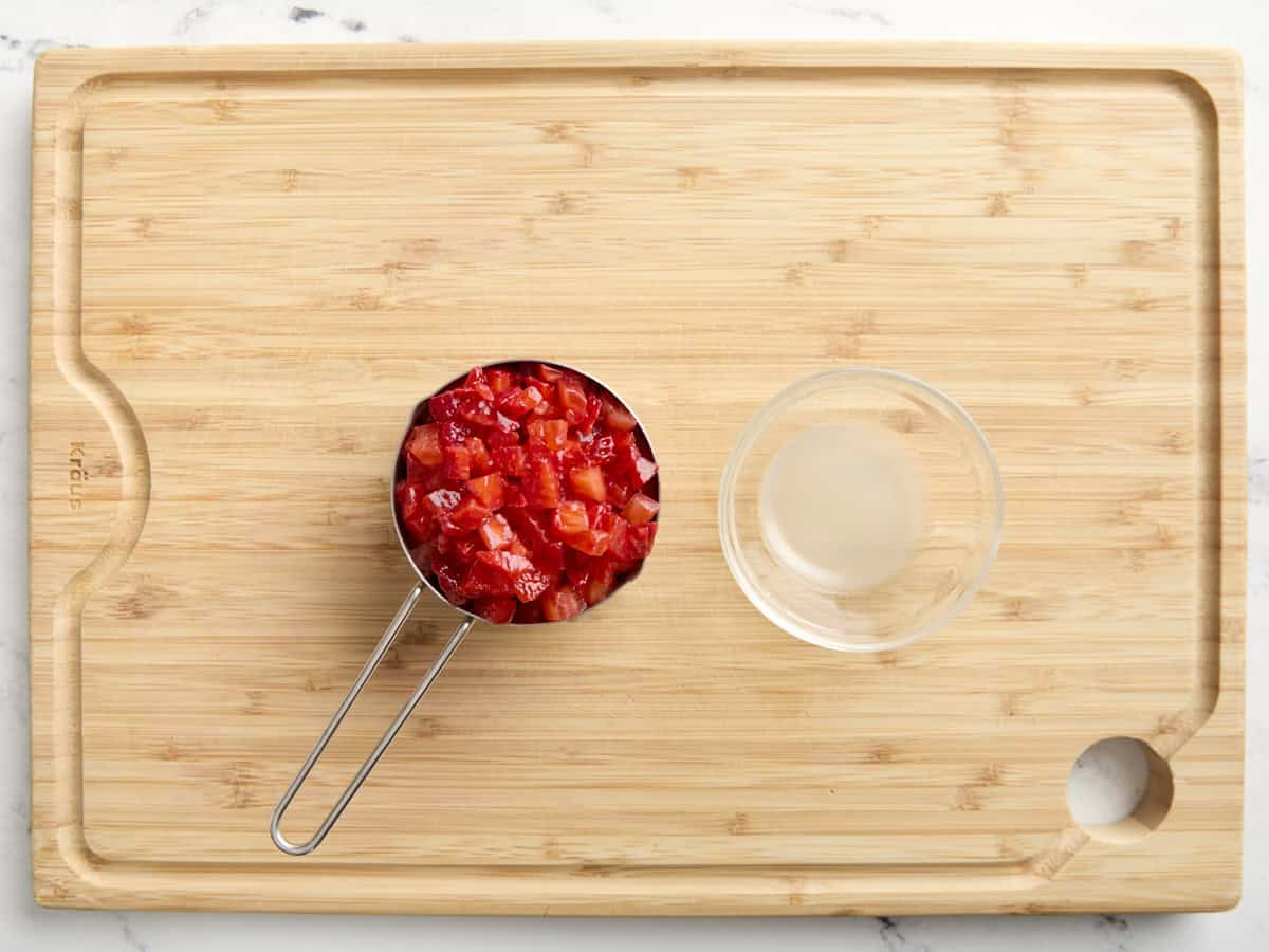 fraises coupées en dés dans une tasse à mesurer à côté d'un petit bol de jus de citron sur une planche à découper.