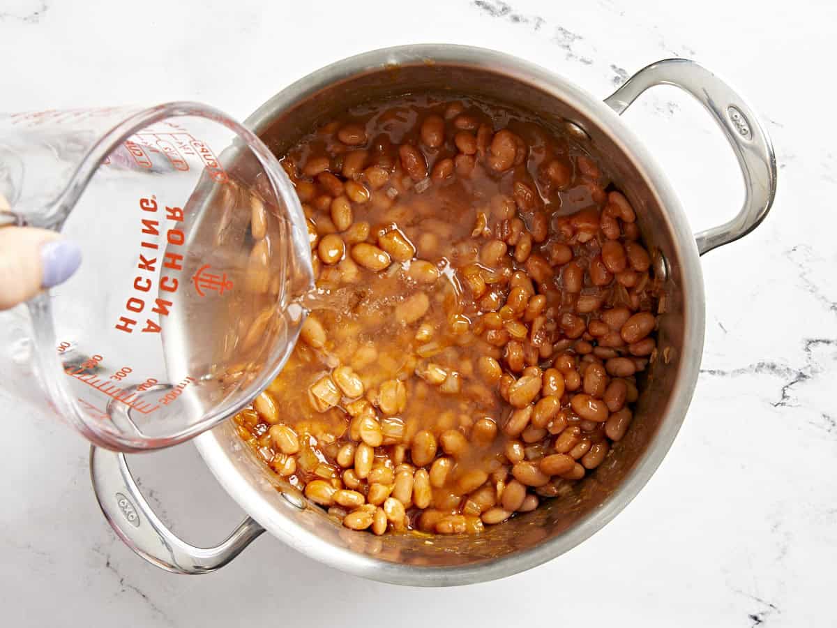 verser de l'eau sur des haricots cuits au four dans une casserole.