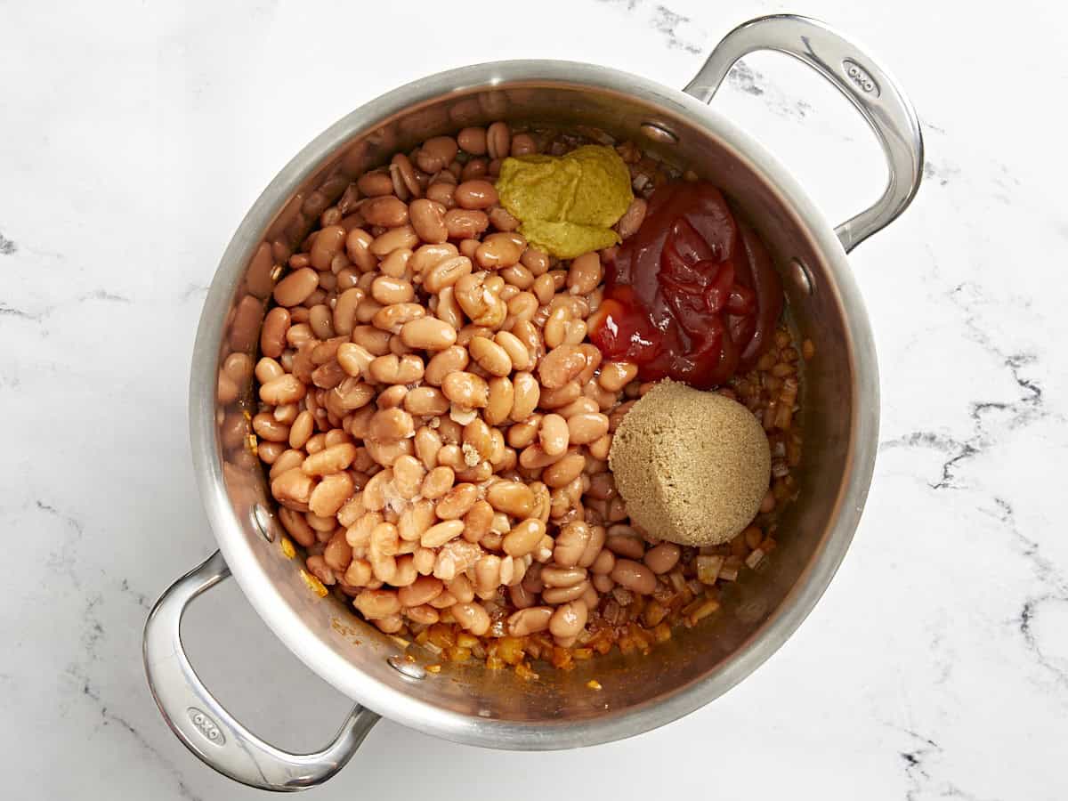 haricots, cassonade, ketchup et moutarde ajoutés à une casserole avec des oignons sautés.