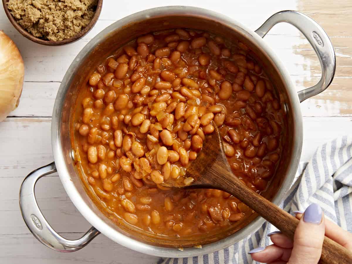 remuer une casserole de haricots cuits au four avec une cuillère en bois.