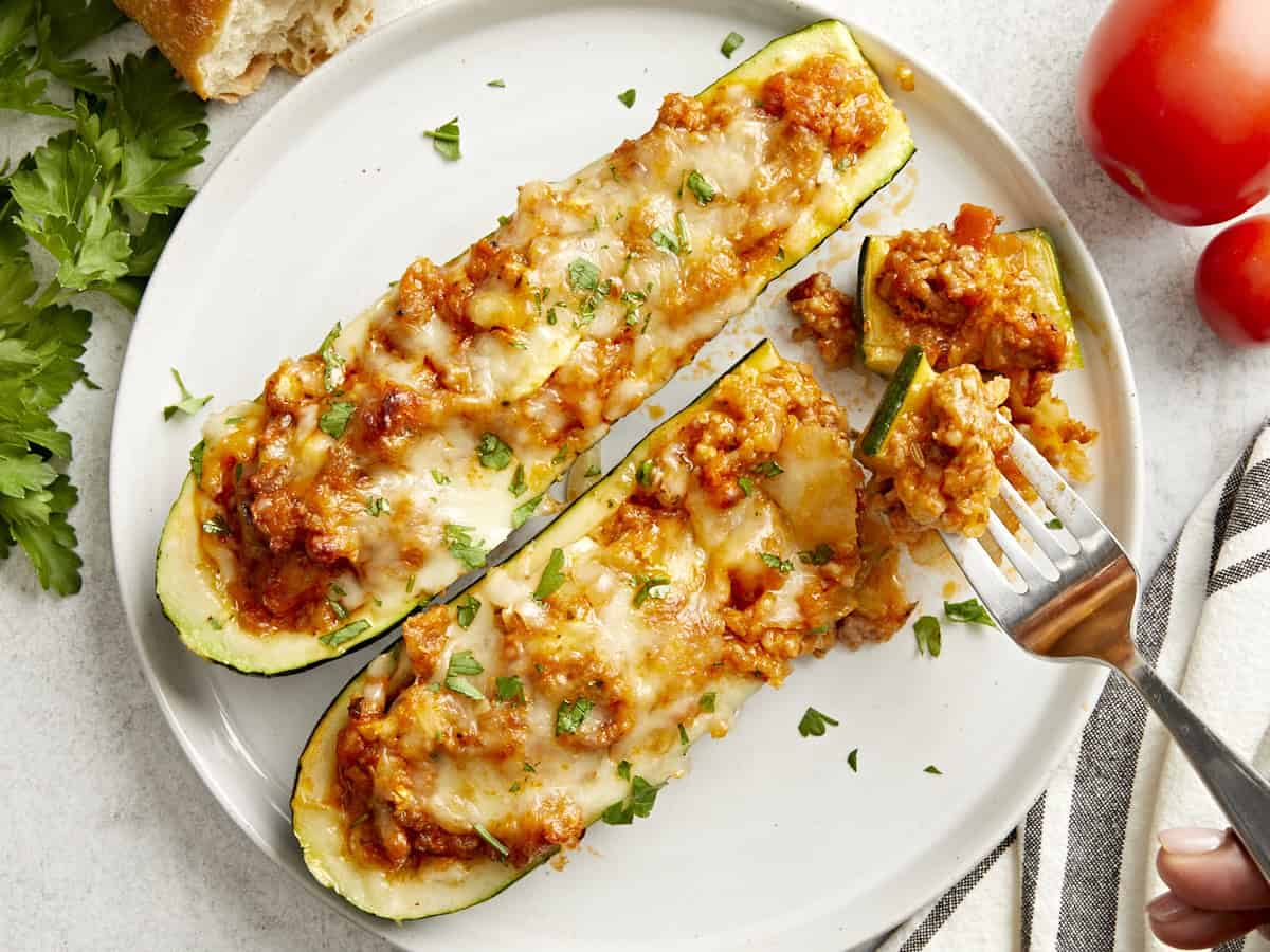 Vue aérienne de deux bateaux de courgettes sur une assiette avec une fourchette qui en ramasse quelques-uns.