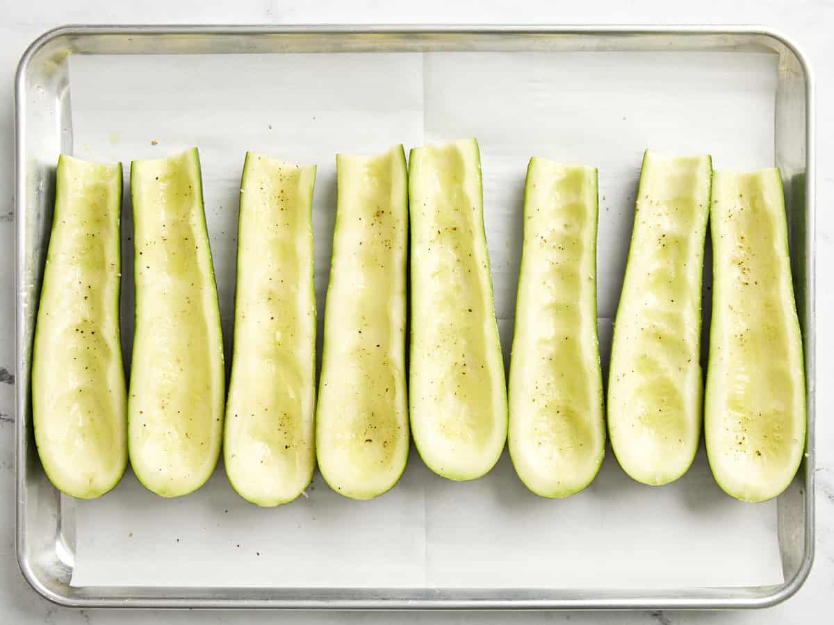 Courgettes évidées, coupées en deux et assaisonnées sur une plaque à pâtisserie recouverte de papier sulfurisé. 