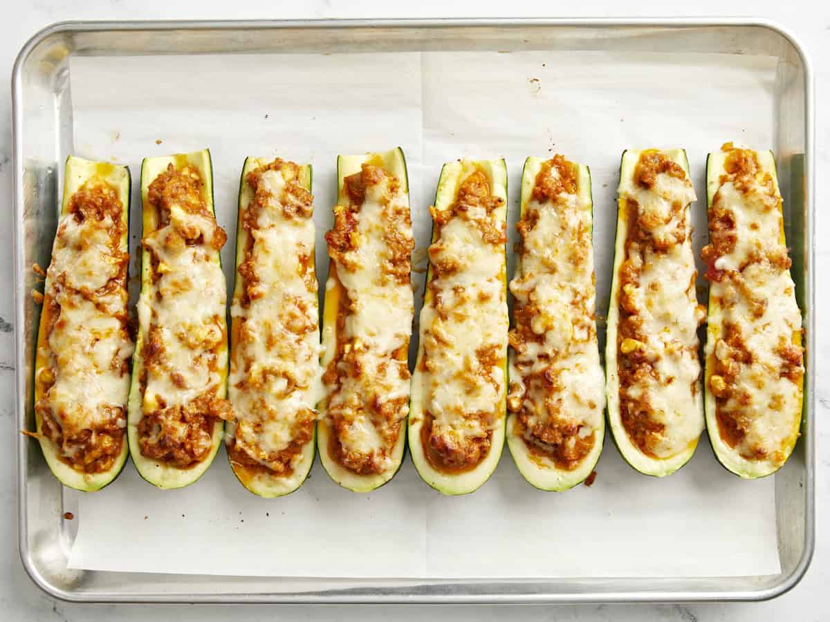 Bateaux de courgettes cuits sur une plaque à pâtisserie recouverte de papier sulfurisé.