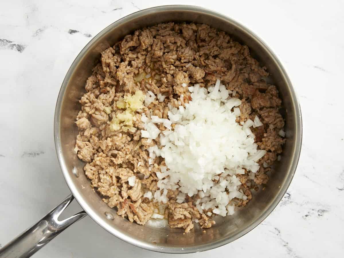 Saucisse italienne dorée, oignon coupé en dés et ail émincé dans une poêle.