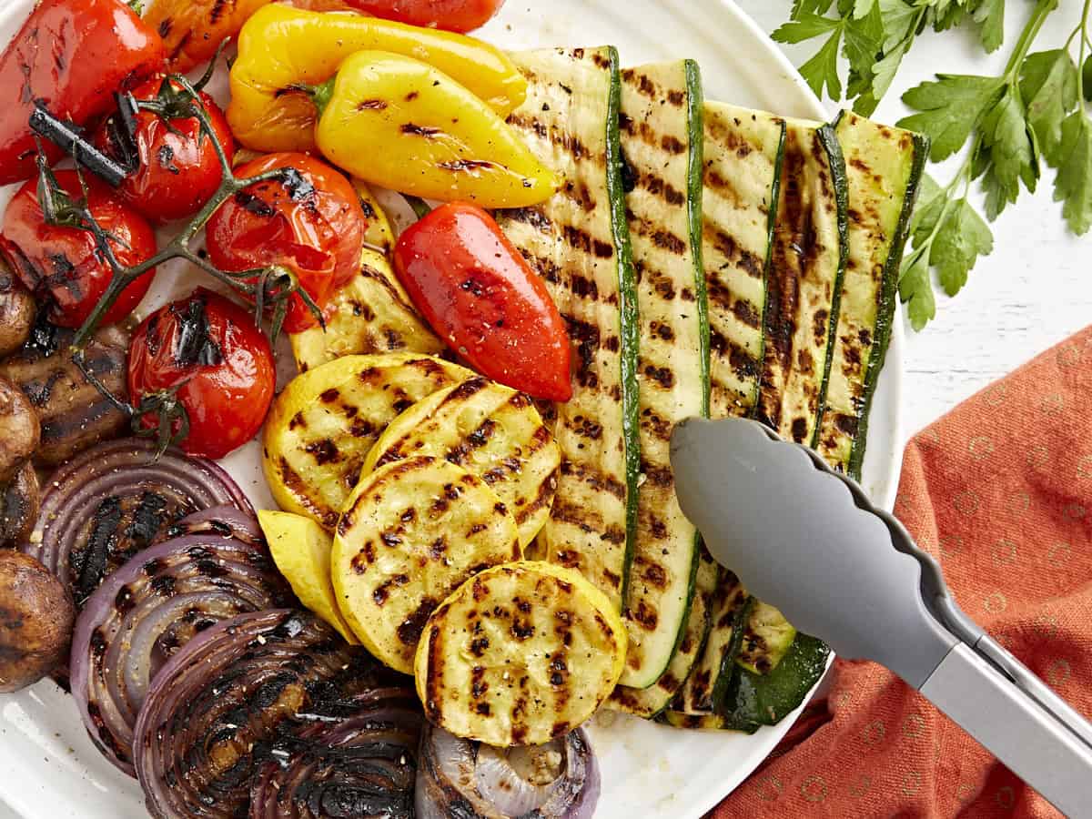 Vue aérienne d'une assiette de légumes grillés avec des pinces saisissant les courgettes.