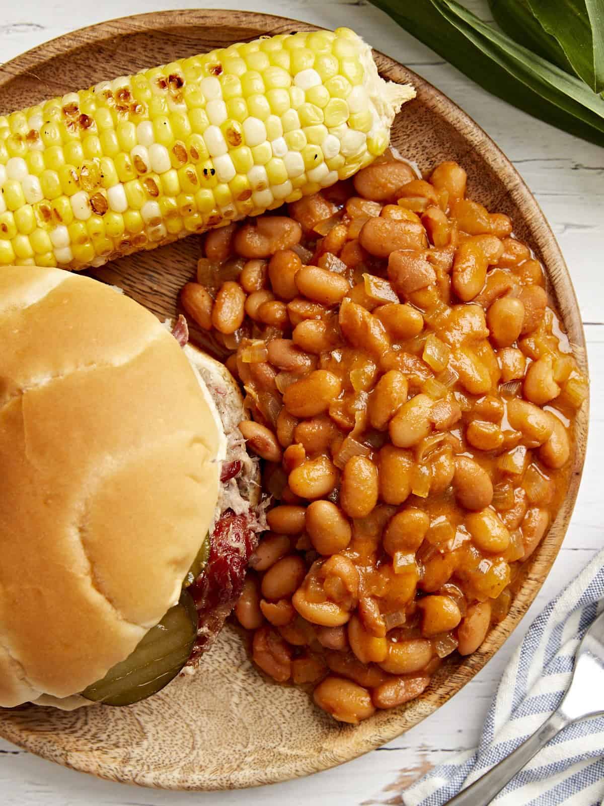 vue aérienne d'une portion de haricots cuits au four sur une assiette avec un sandwich et des épis de maïs.