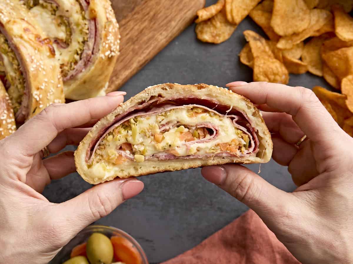 Mains tenant une tranche de muffaletta roulée