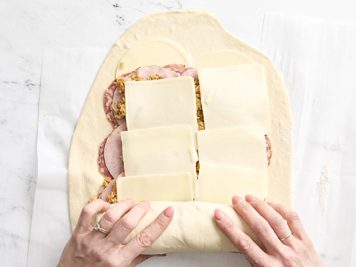 Mains enroulant la pâte à pizza sur la garniture pour les rouleaux de muffaletta