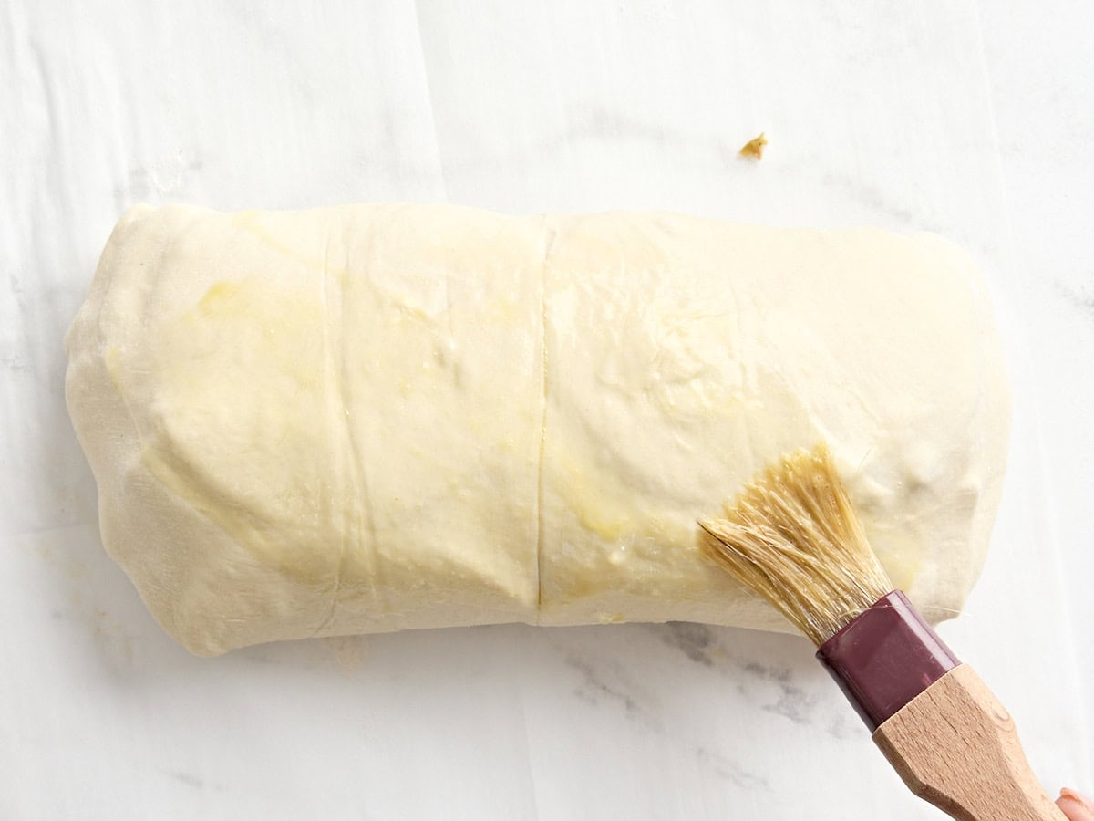 Un pinceau a ajouté une dorure à l'œuf à un rouleau de muffaletta non cuit