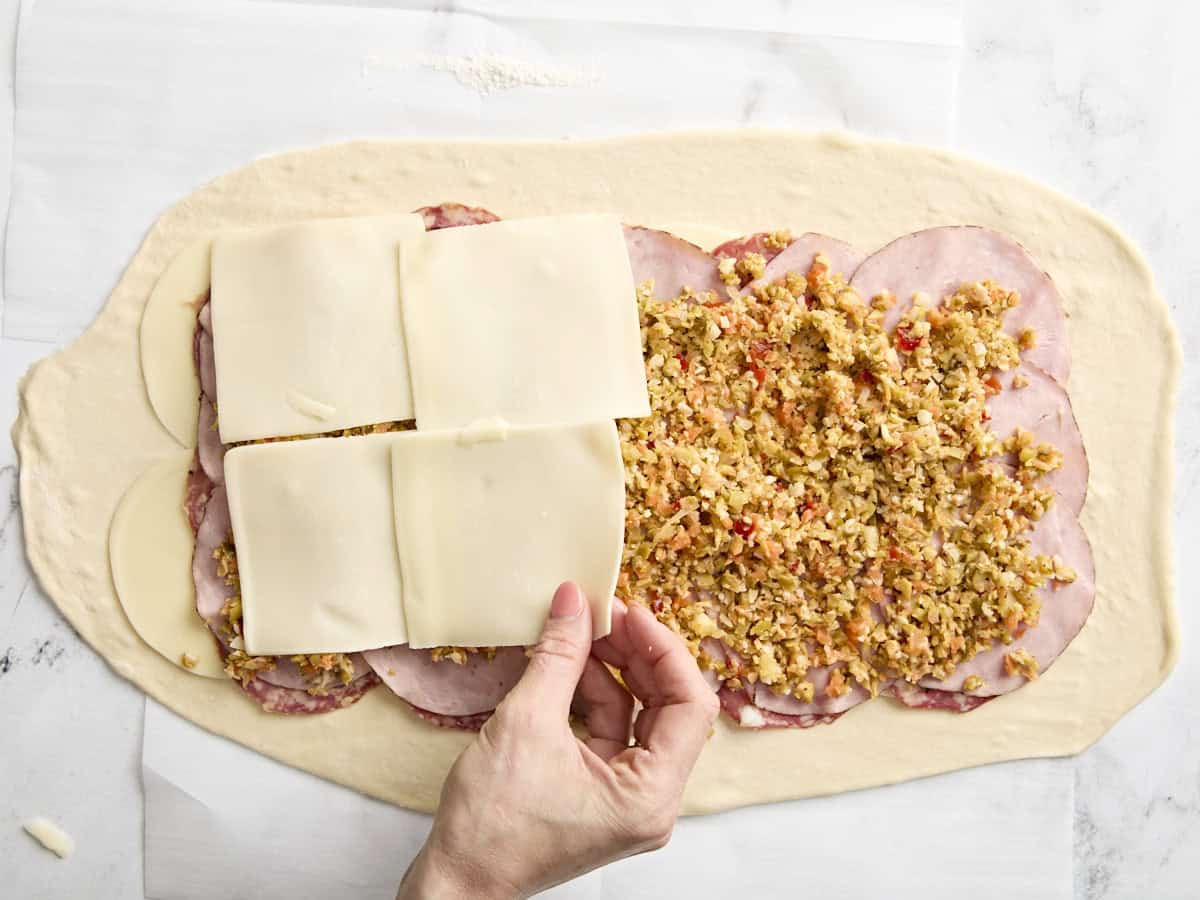 Ajout de la dernière couche de fromage à un rouleau de muffaletta