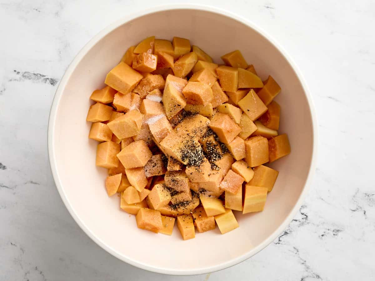Cubes de courge musquée dans un bol allant au four avec de la poudre d'ail, du sel et du poivre noir.
