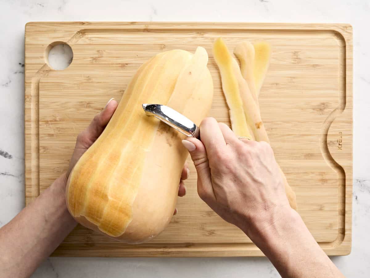 Une main épluchant une courge musquée avec un éplucheur de légumes.