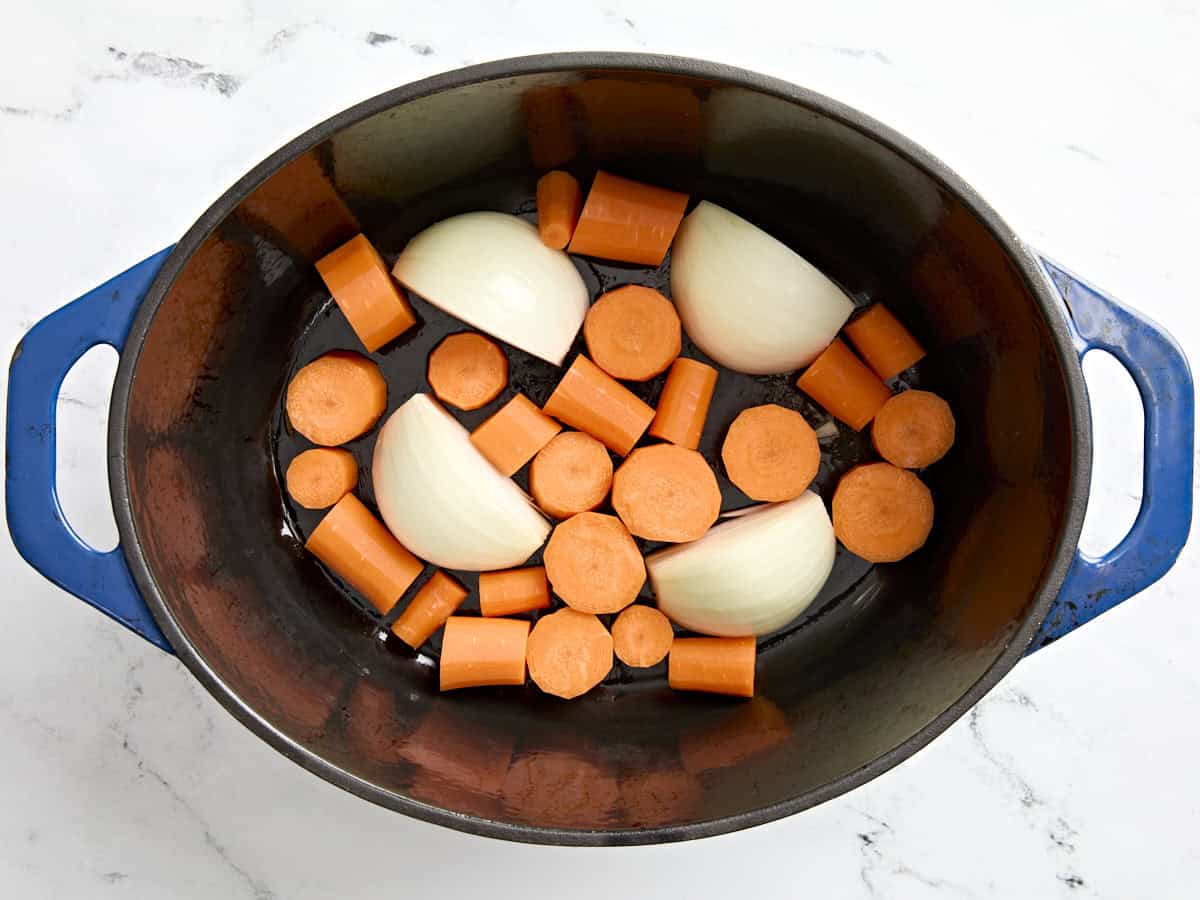 Oignons et carottes tranchés ajoutés à une cocotte.