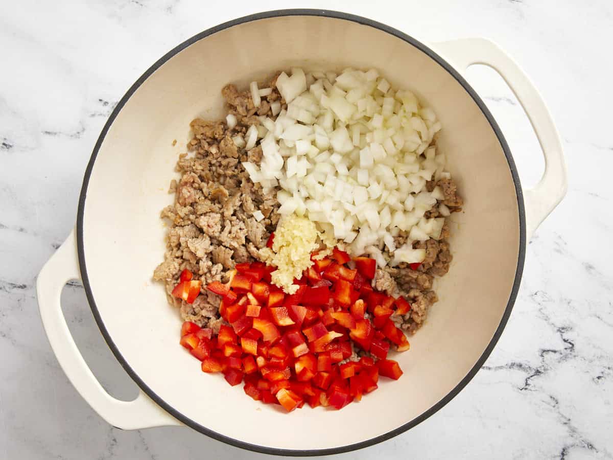 Saucisse italienne, oignons, ail et poivron rouge dans une cocotte.