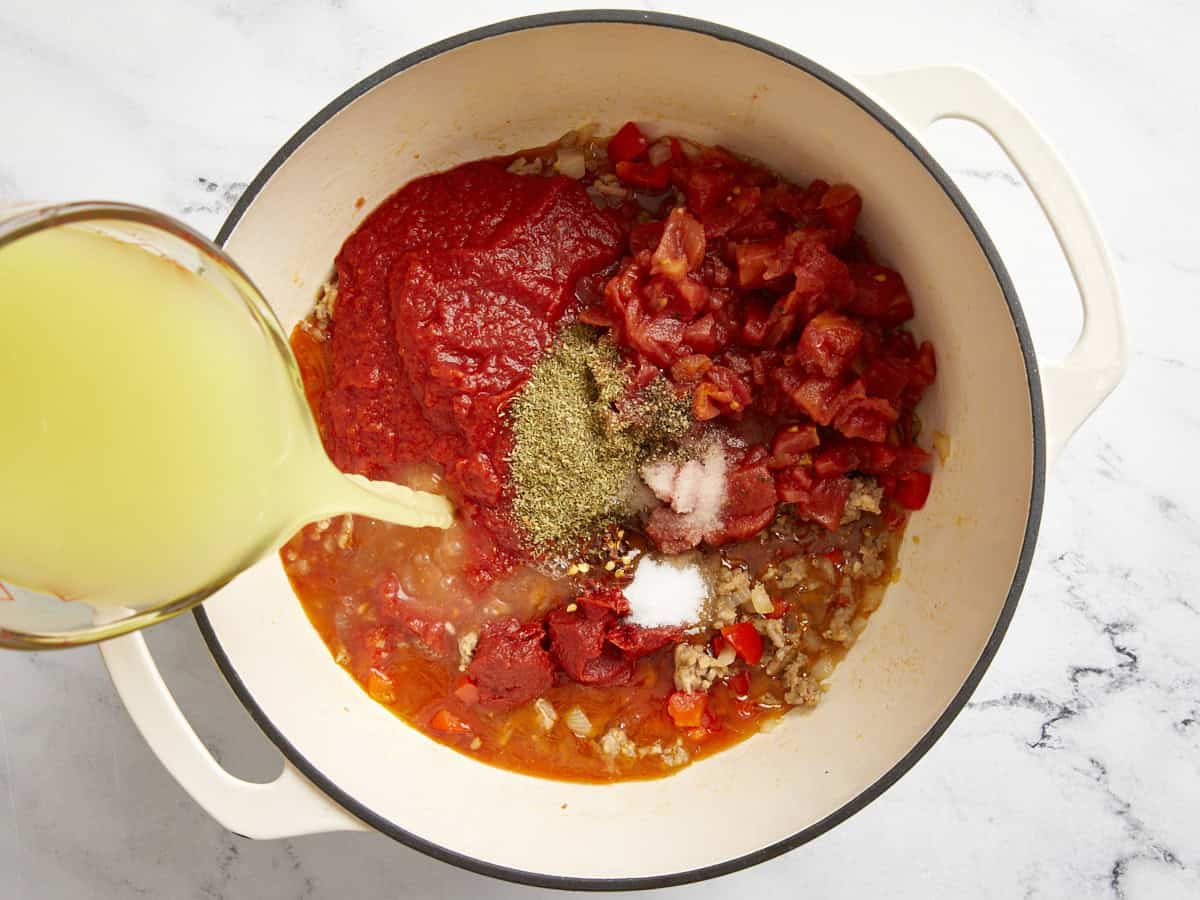 Tomates, épices et bouillon de poulet ajoutés à la marmite.