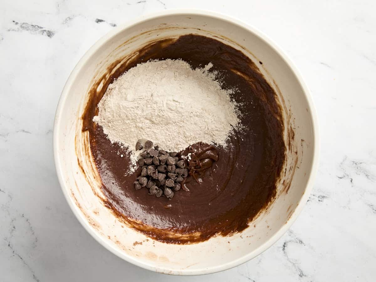 Ingrédients secs et pépites de chocolat ajoutés au mélange de chocolat humide dans un bol à mélanger.