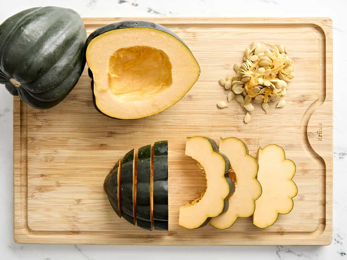 Une moitié de courge poivrée épépinée sur une planche à découper et l'autre moitié coupée en tranches.